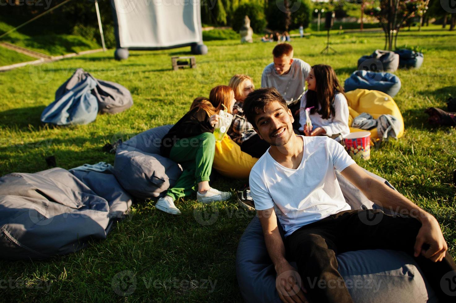 Young multi ethnic group of people watching movie at poof in open air cinema. Close up portrait of funny guy. photo