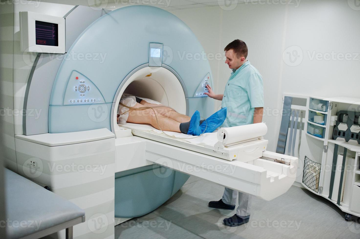 Male doctor turns on magnetic resonance imaging machine with patient inside. photo