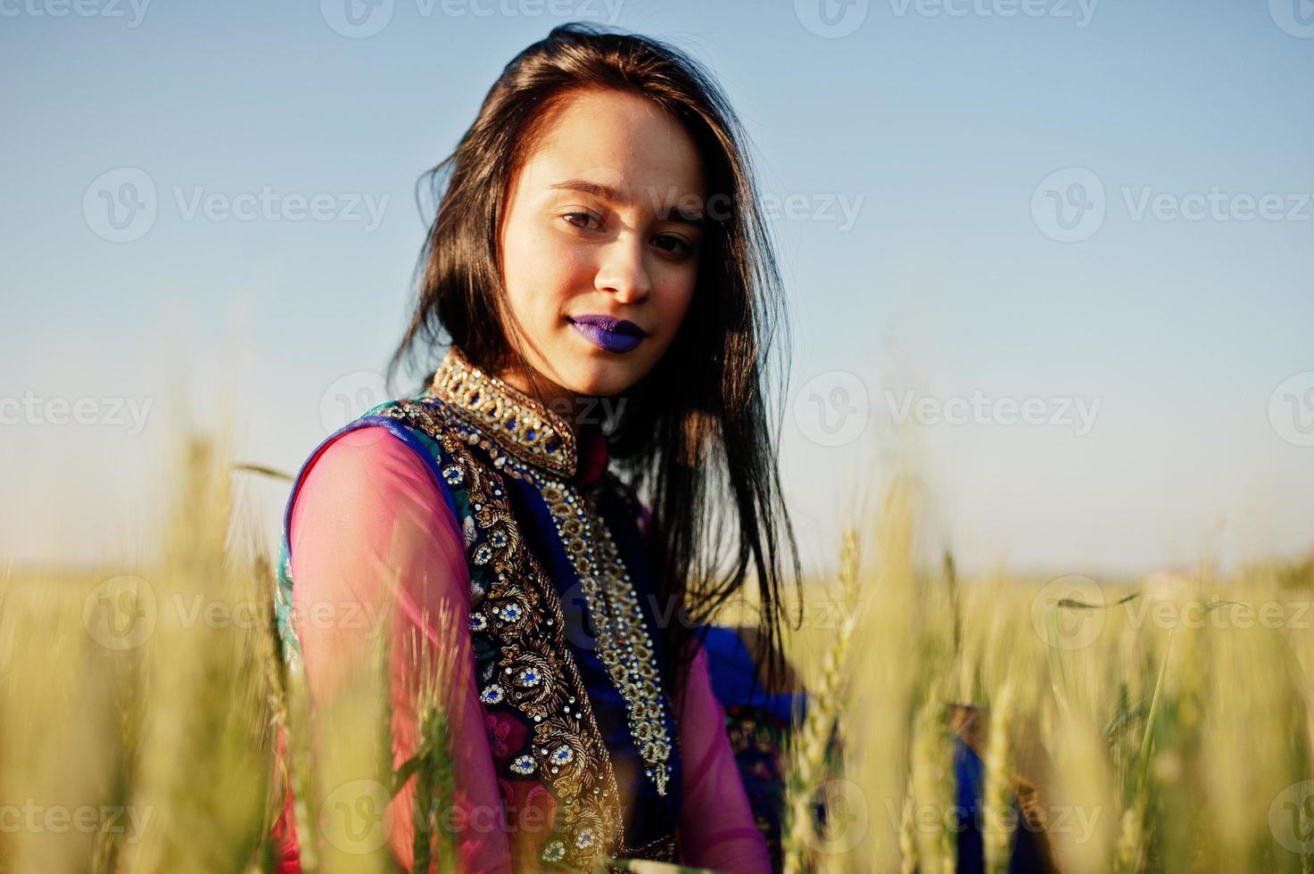 tierna niña india en sari, con maquillaje de labios violetas posada en el campo al atardecer. modelo indio de moda. foto