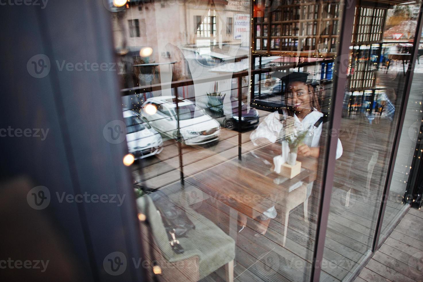 African american woman in overalls and beret sitting on cafe against glass window. photo