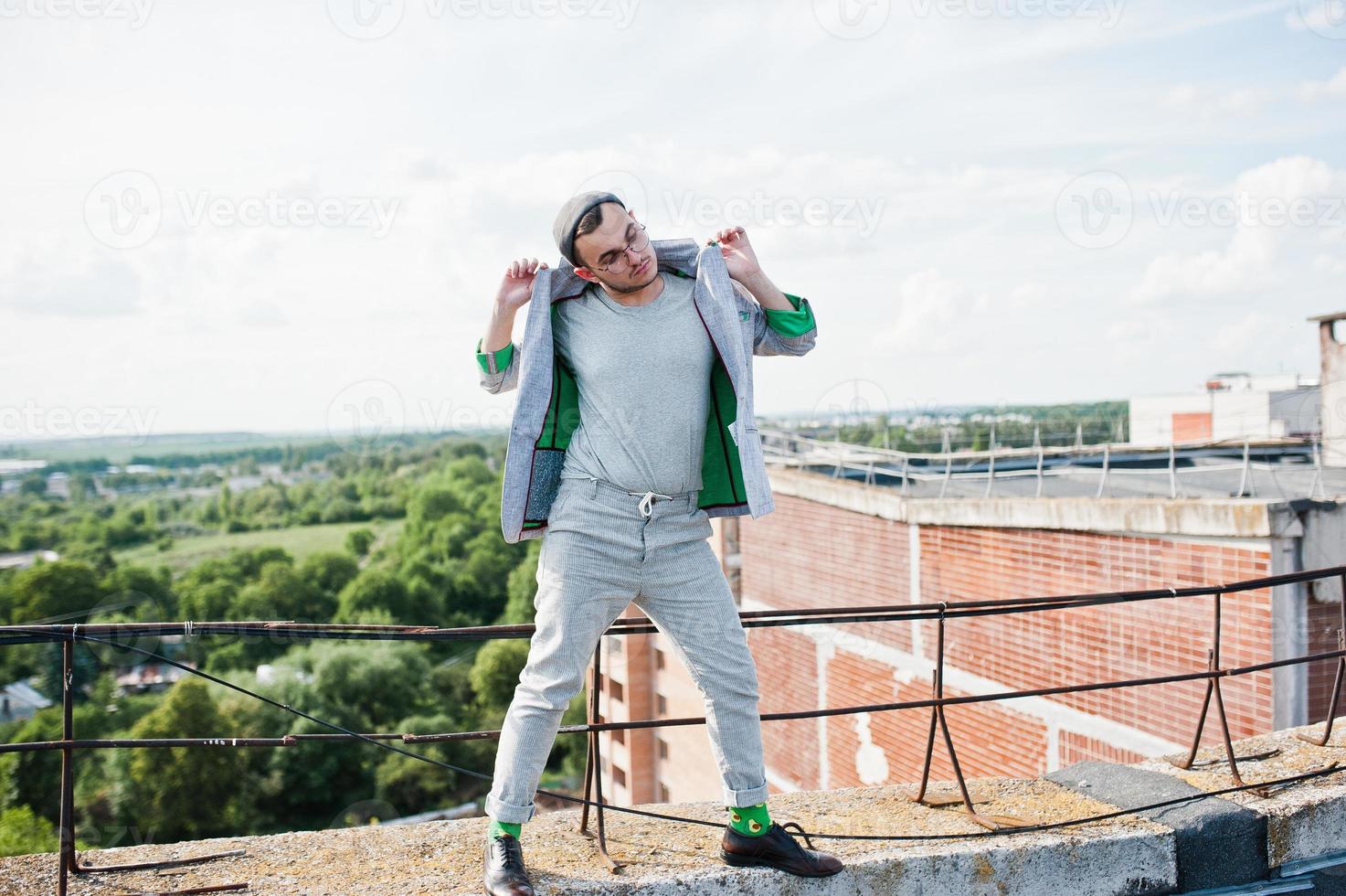 Dreamer stylish macho man in gray suit, hat and glasses posed on the roof. photo