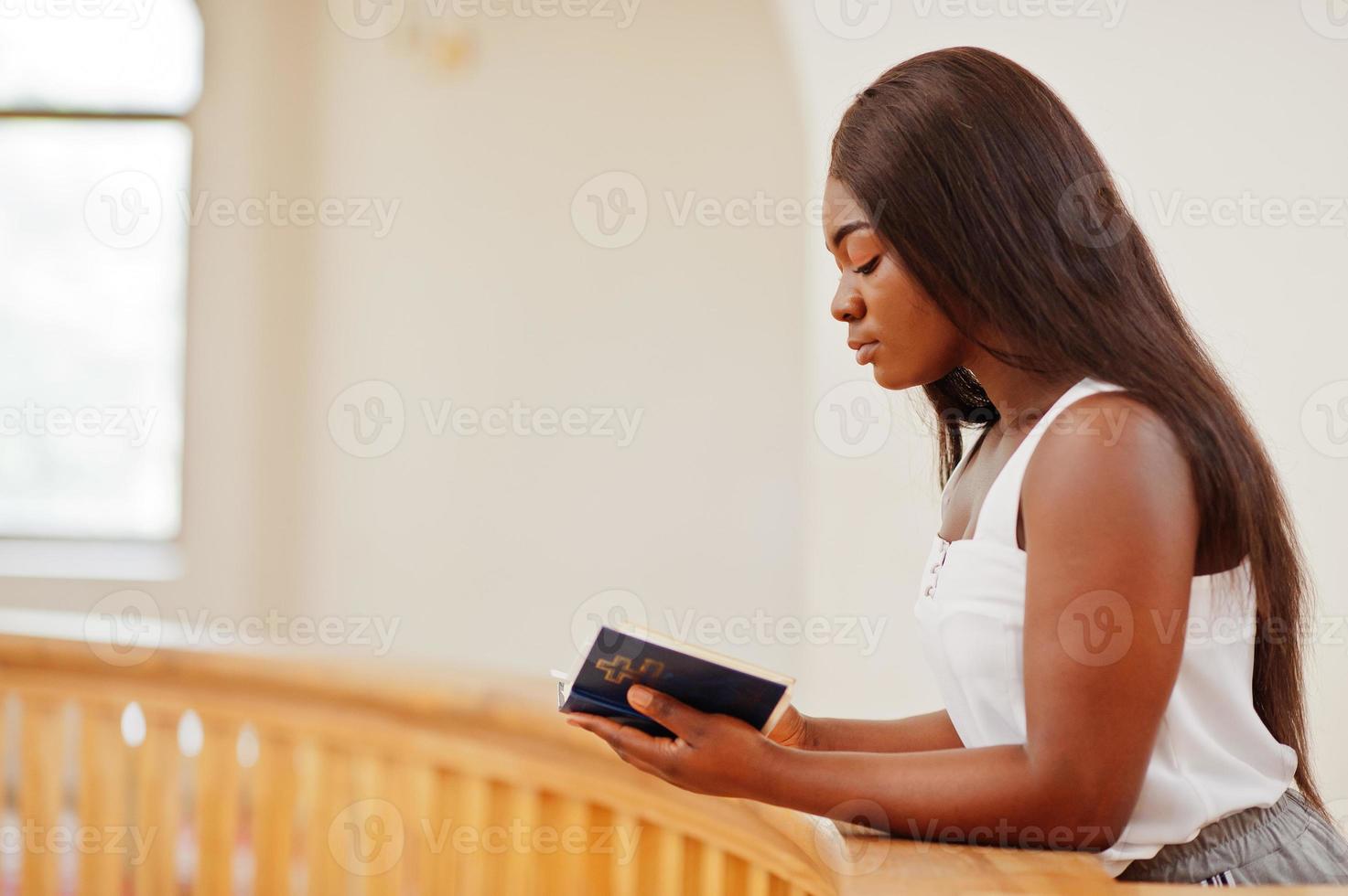 mujer afroamericana rezando en la iglesia. los creyentes meditan en la catedral y tiempo espiritual de oración. chica afro con la santa biblia en las manos. foto