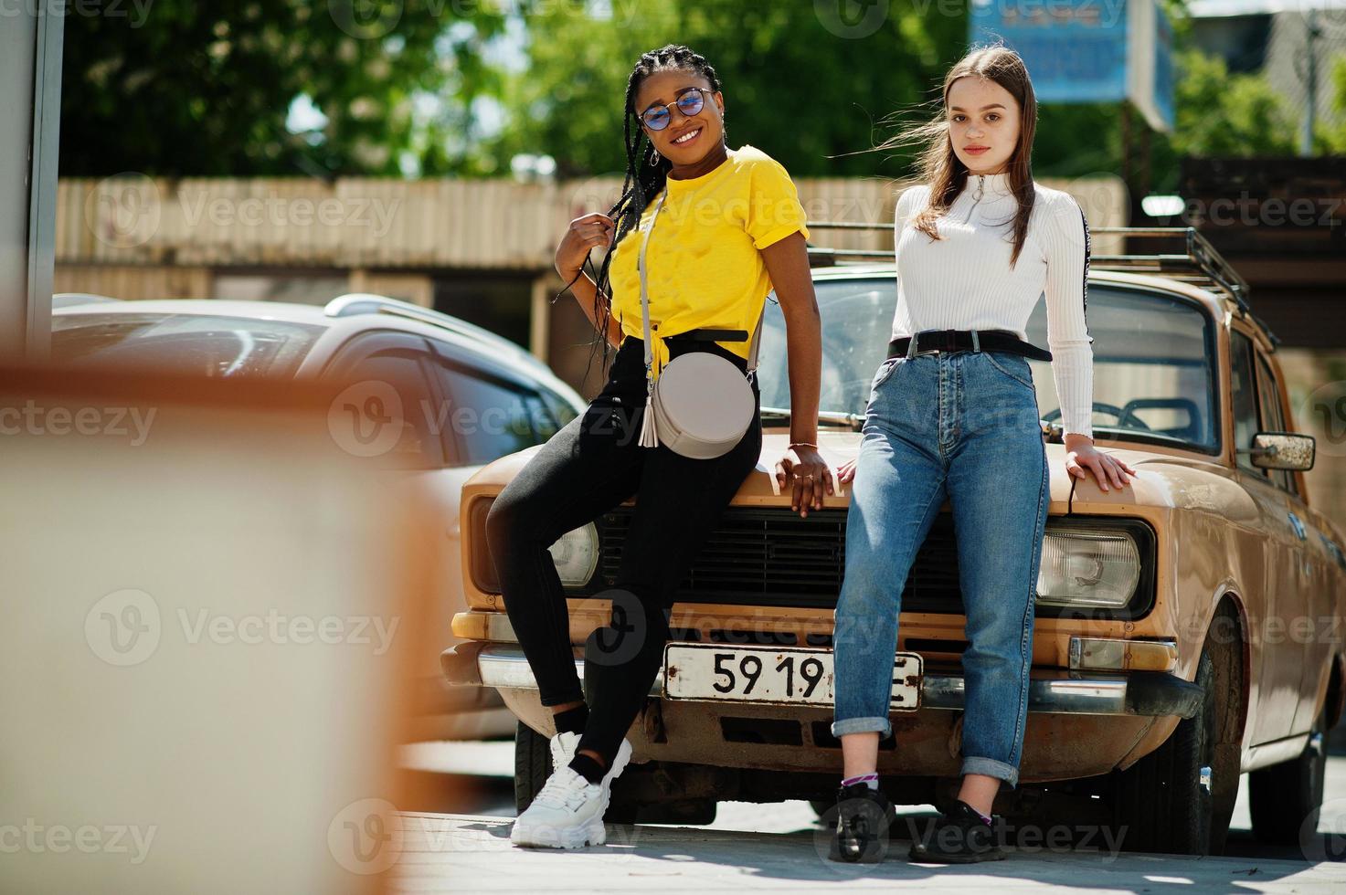White caucasian girl and black African American together against old retro car. World unity, racial love, understanding in tolerance and races diversity cooperation. photo