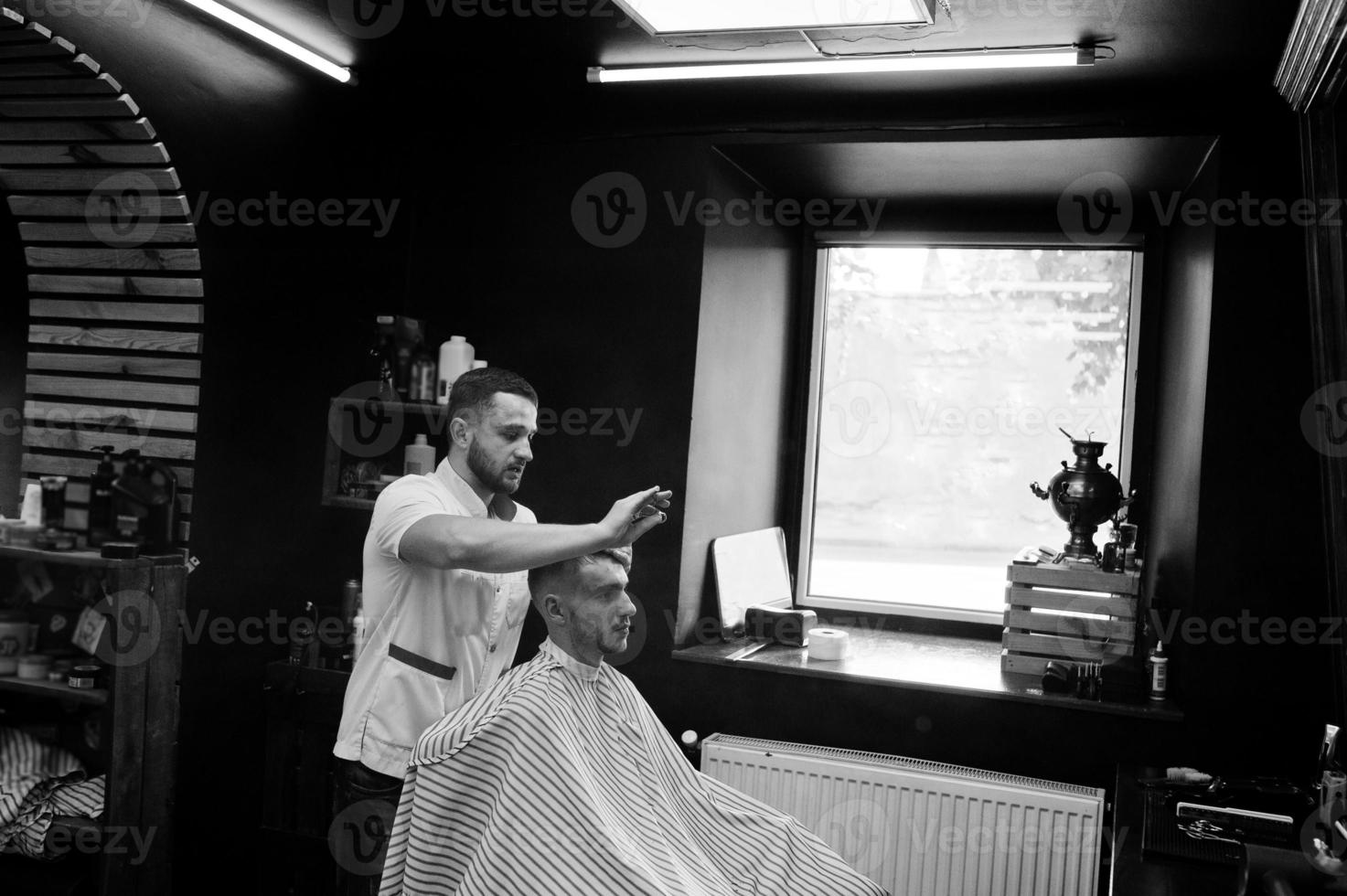 un joven barbudo que se corta el pelo con un peluquero mientras se sienta en una silla en la barbería. alma de barbero. foto