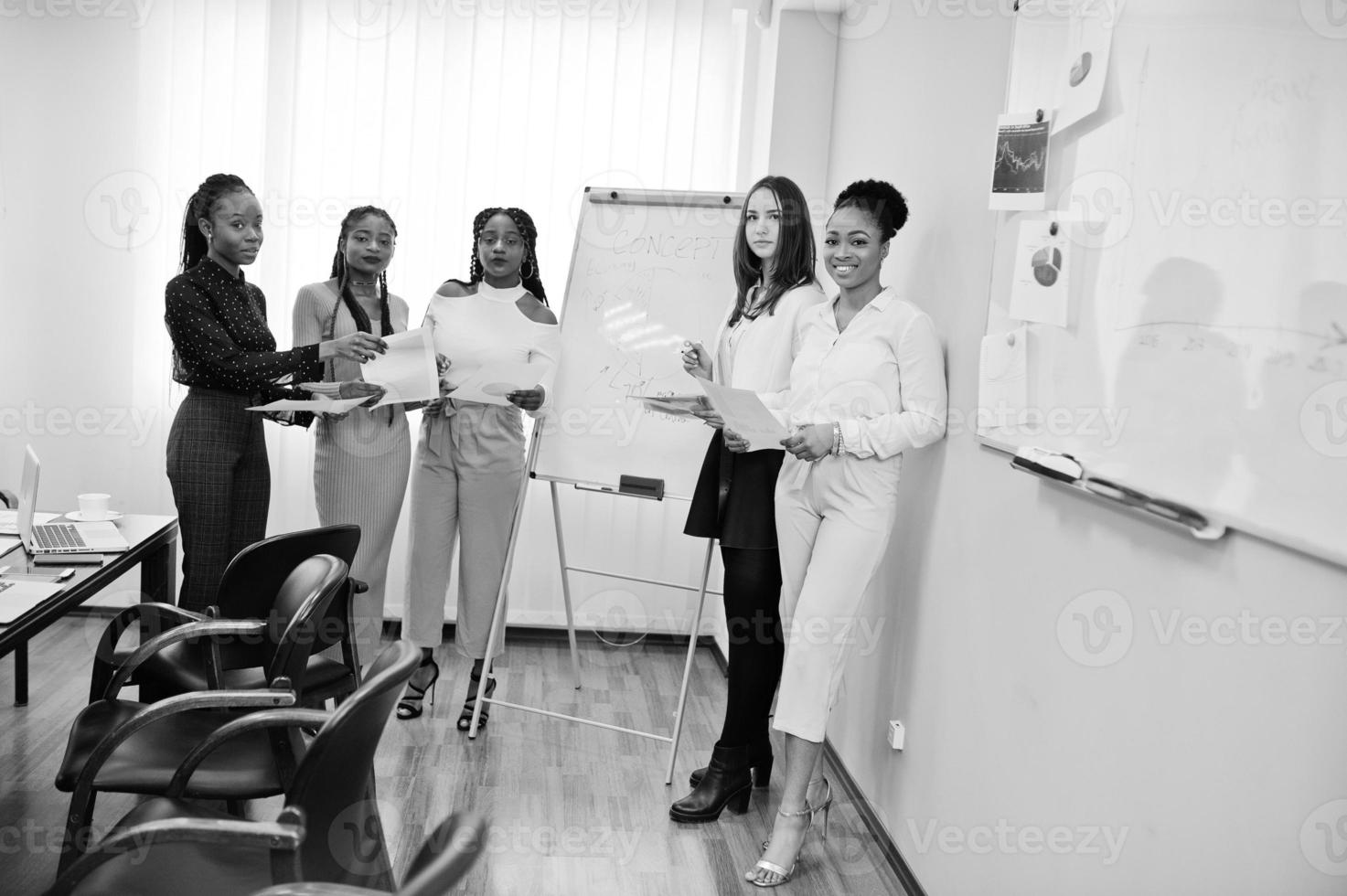 Multiracial women colleagues, crew of divercity female partners in office standing near flipchart. photo