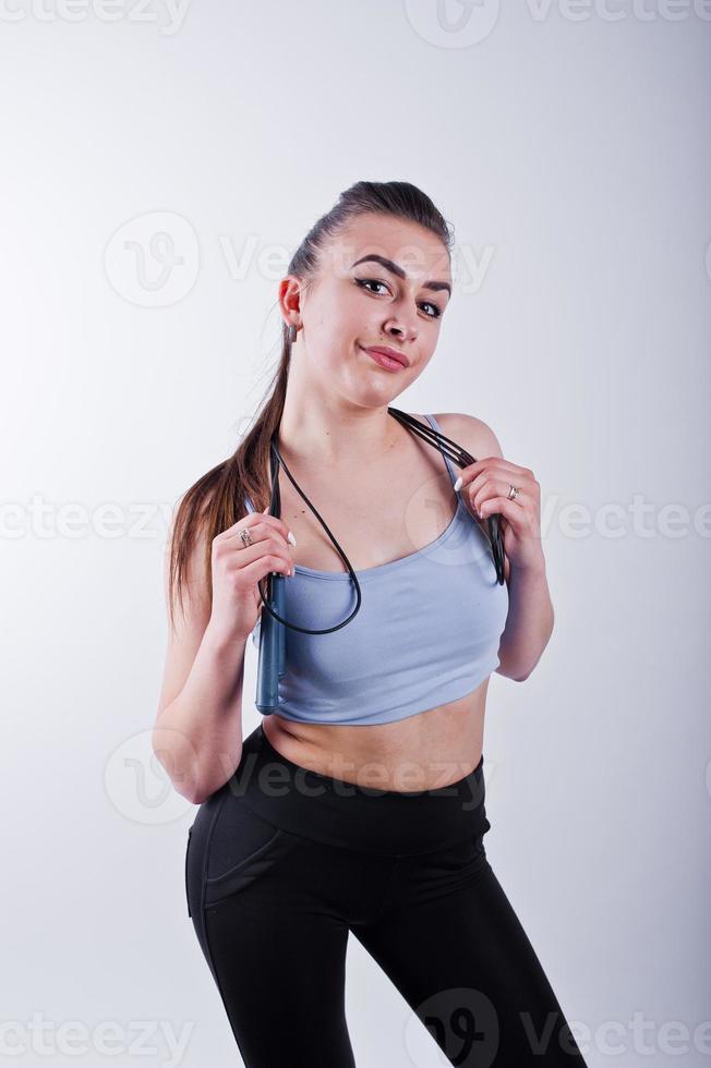 Cheerful attractive young fitness woman in top and black leggings with jump rope isolated over white background. photo