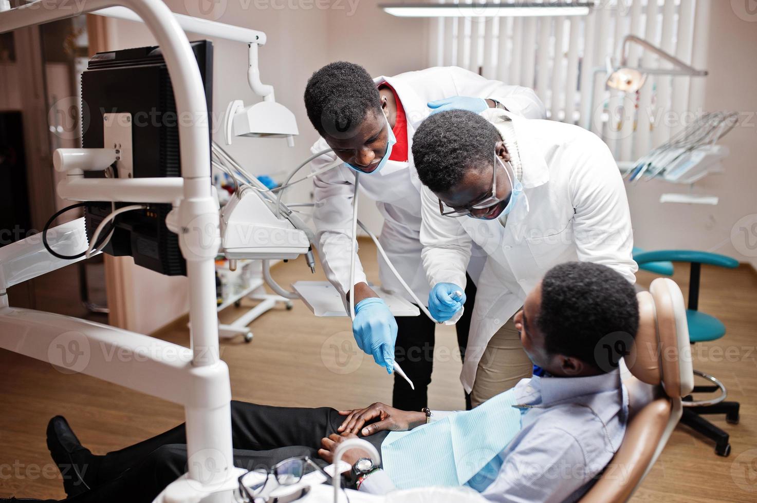 African american man patient in dental chair. Dentist office and doctor practice concept. Professional dentist helping his patient at dentistry medical. Drilling patient's teeth in clinic. photo