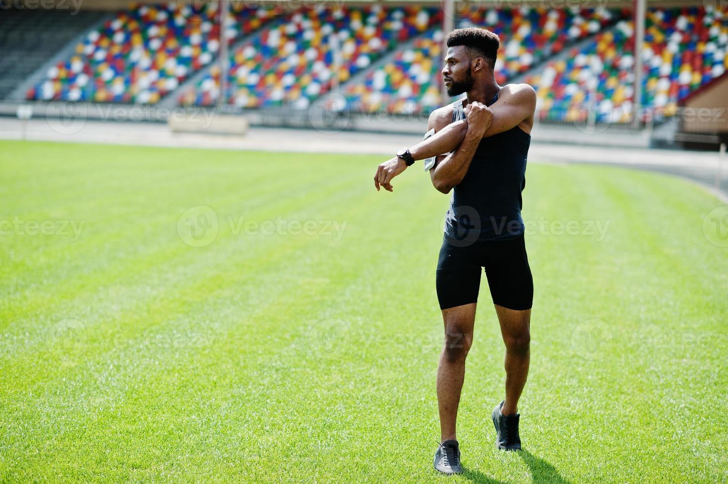 African american male athlete in sportswear doing stretching exercise at stadium. photo