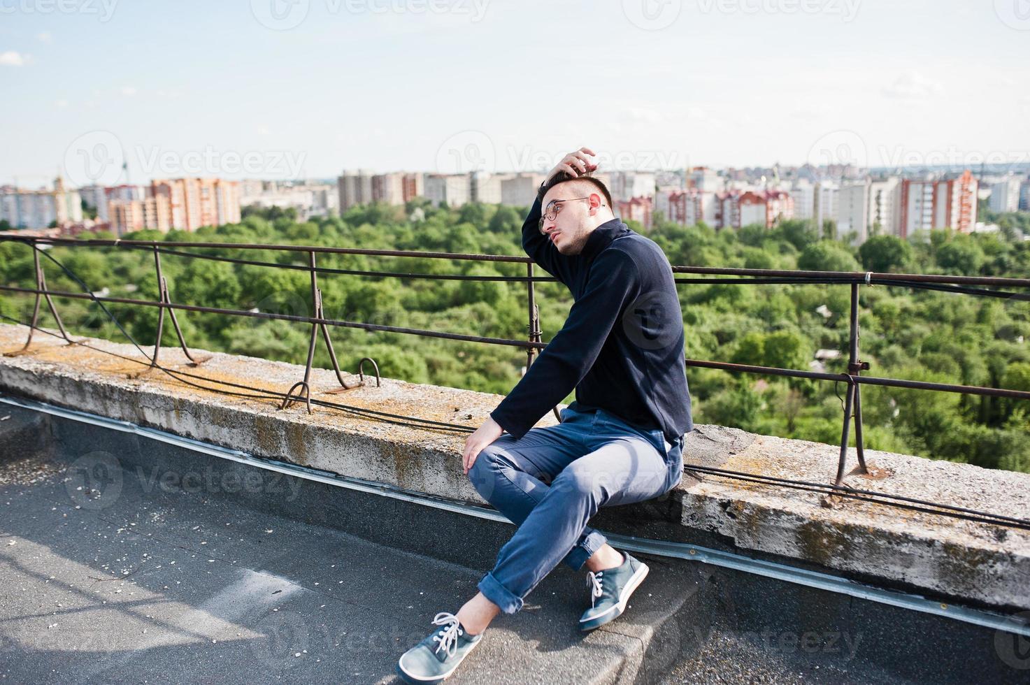 Dreamer stylish macho man in black golf and glasses posed on the roof. photo