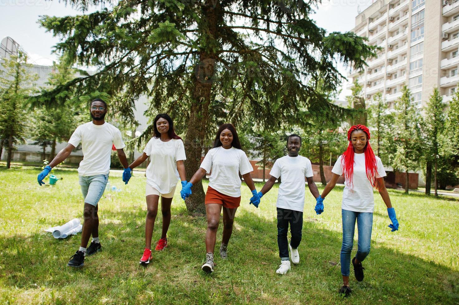 Group of happy african volunteers hold hands together in park. Africa volunteering, charity, people and ecology concept. photo