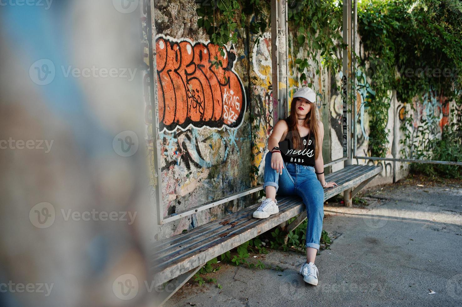 elegante chica hipster casual con gorra y jeans contra una gran pared de graffiti. foto