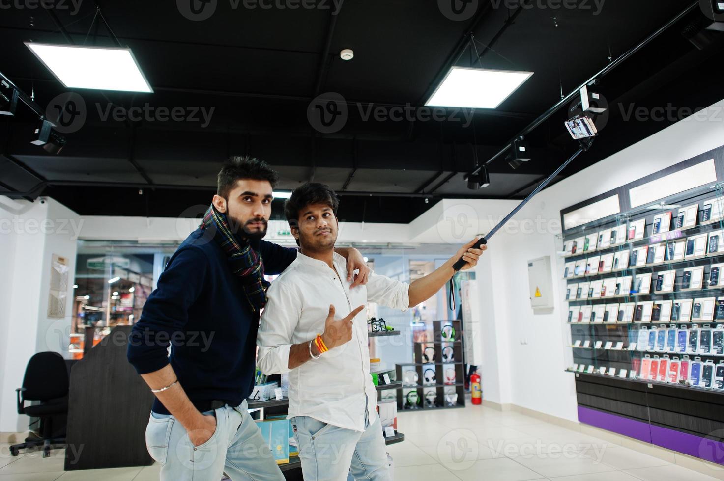 Two indians mans customer buyer at mobile phone making selfie by monopod stick. South asian peoples and technologies concept. Cellphone shop. photo