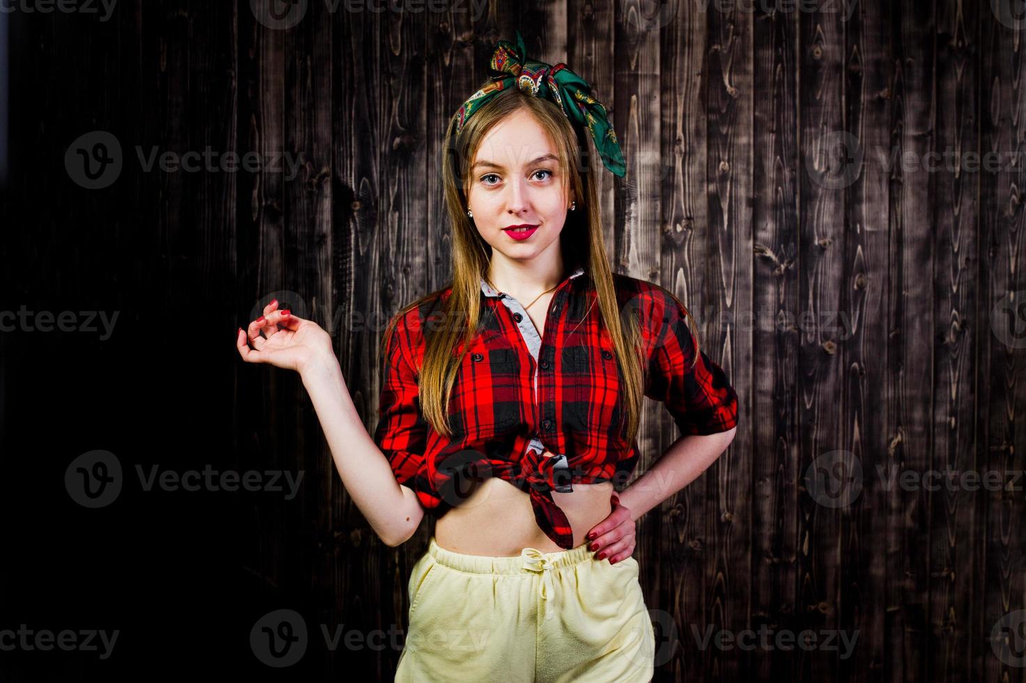 joven ama de casa divertida en camisa a cuadros y pantalones cortos amarillos pin up estilo sobre fondo de madera. foto