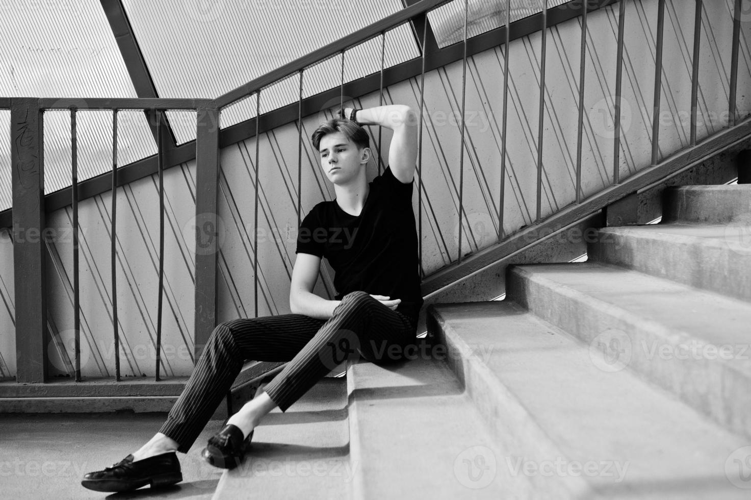 joven macho con estilo en chaqueta negra planteada al aire libre de la calle. increíble modelo de hombre en el tonnel de escaleras rojas. foto