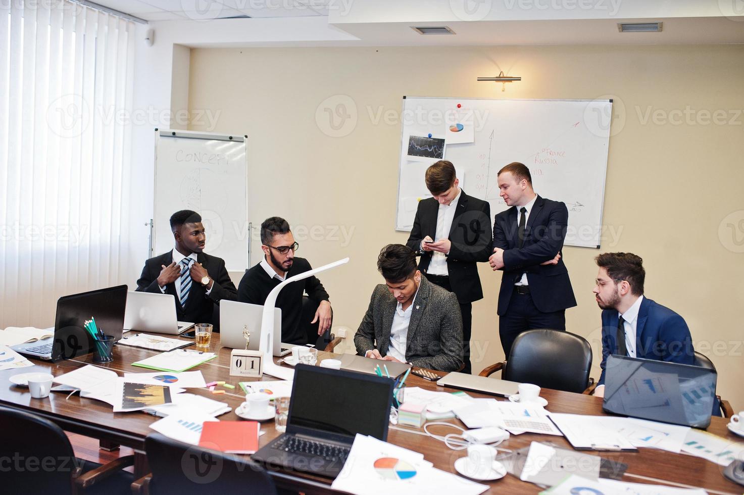 Six multiracial business mans at office at table. Diverse group of male employees in formal wear discussing. photo