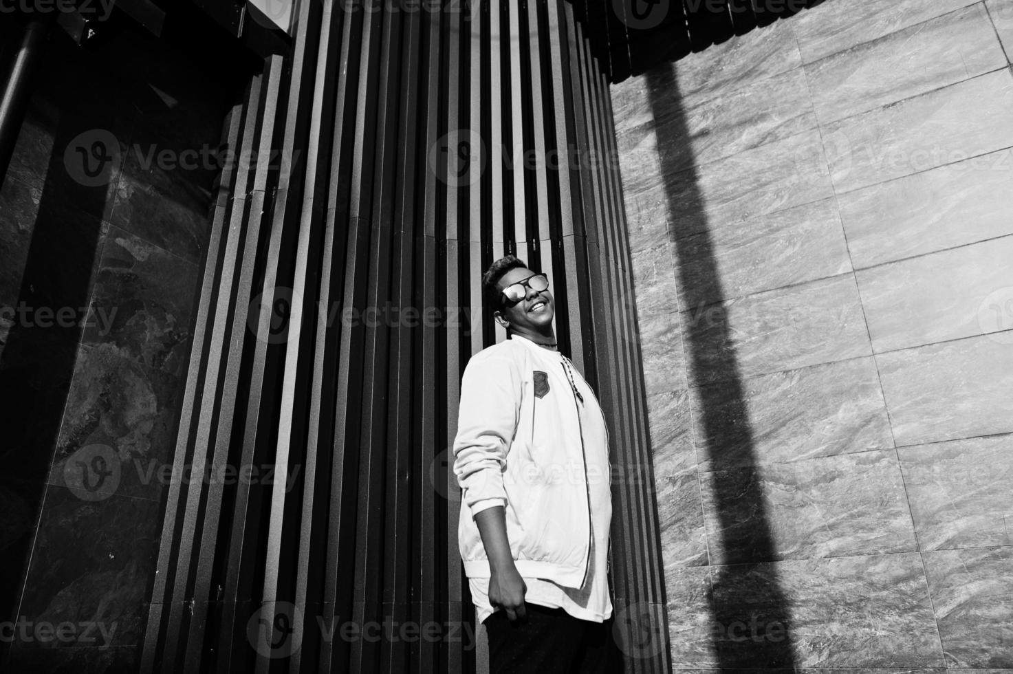 Stylish hipster arab man guy in sunglasses posed outdoor in street at sunset against gray wall. photo