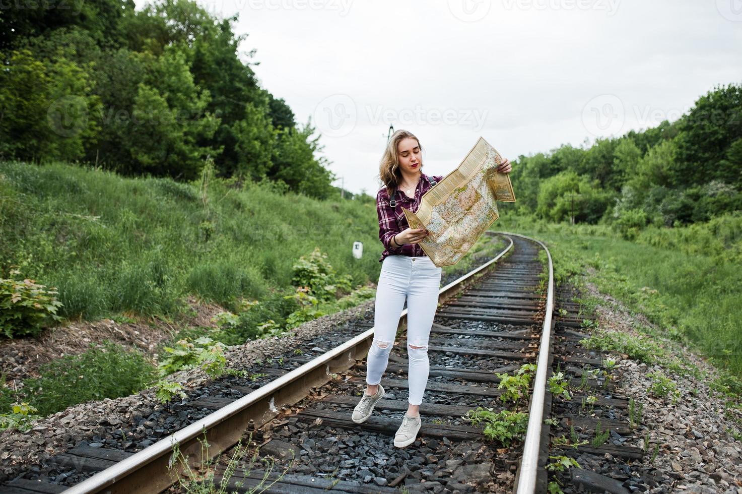 retrato de una linda chica rubia con camisa de tartán caminando por el ferrocarril con un mapa en las manos. foto