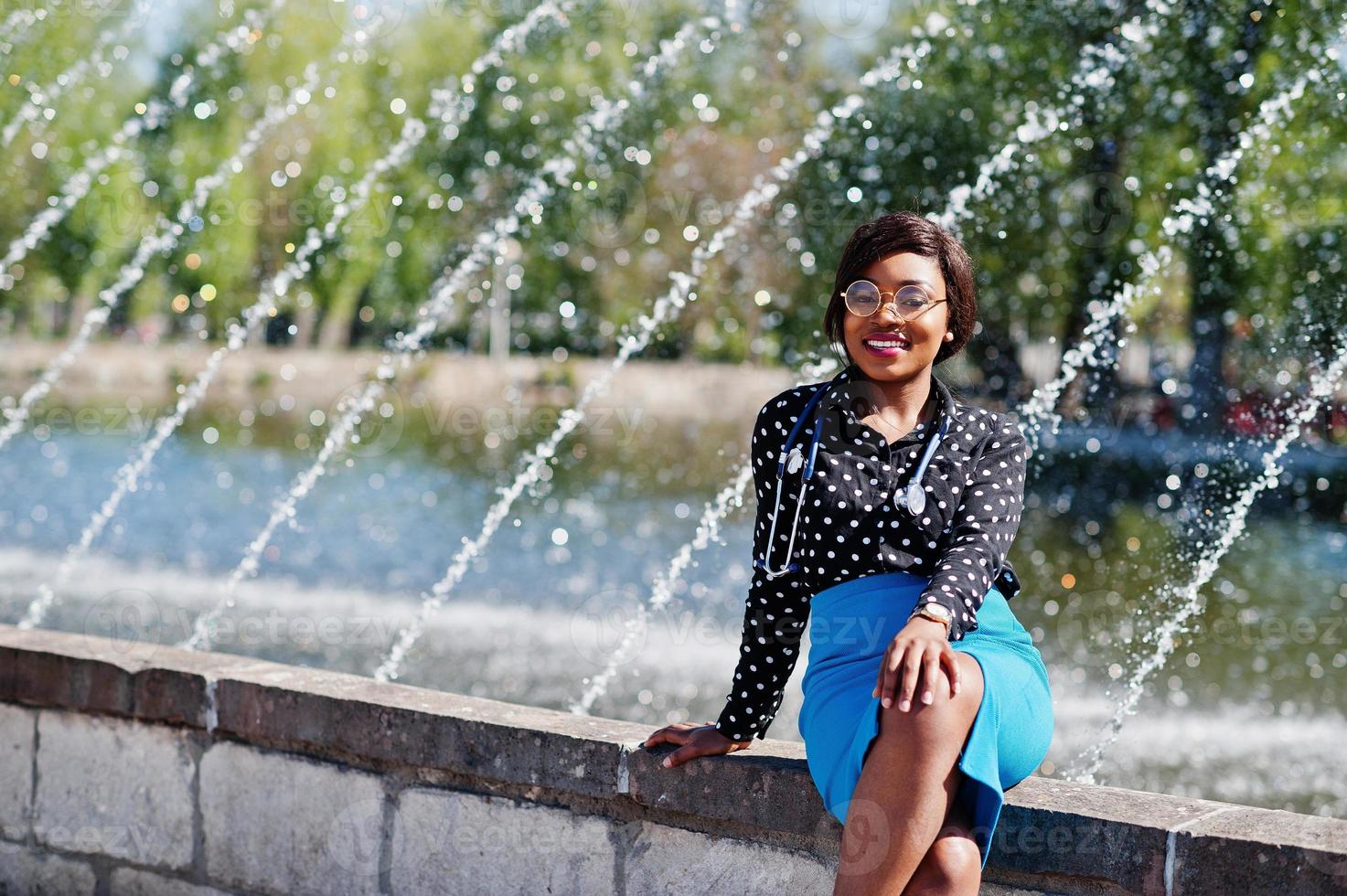 African american doctor female with stethoscope posed outdoor background fountains. photo