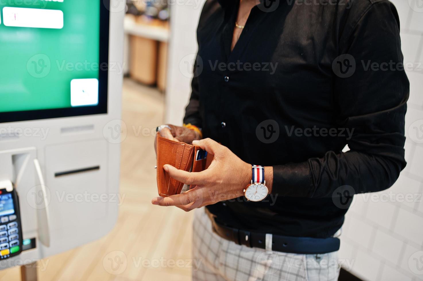 Hands of man customer at store place orders and pay through self pay floor kiosk for fast food, payment terminal. His holding wallet and find credit card. photo