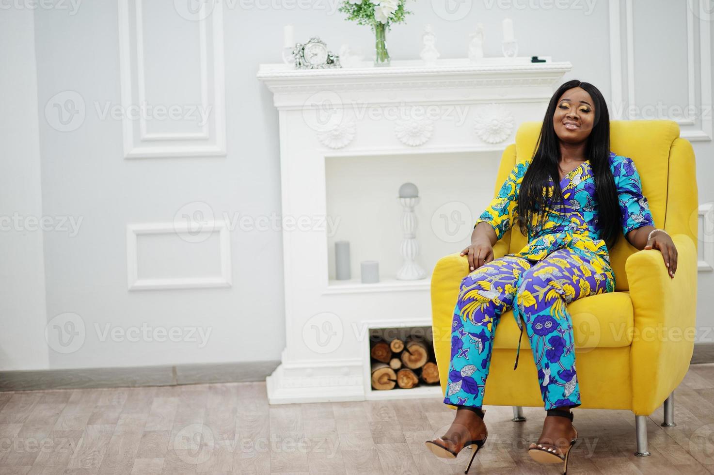 Elegance african american woman model wear in colored clothes. Chic afro women in room sitting on yellow chair. photo