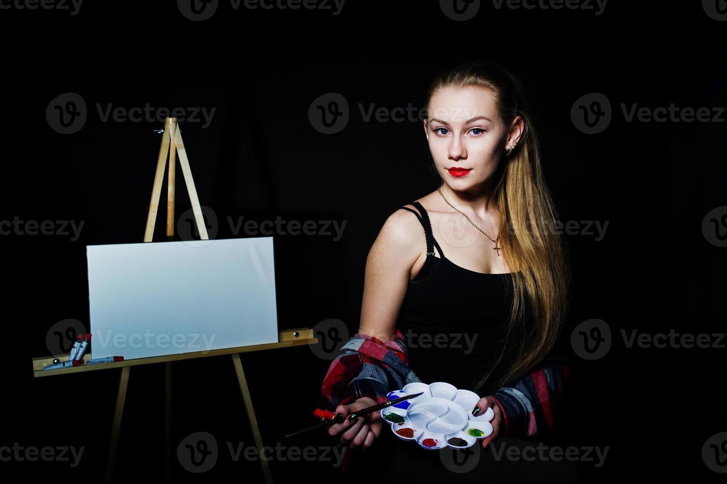 Beautiful woman artist painter with brushes and oil canvas posing in studio isolated on black. photo