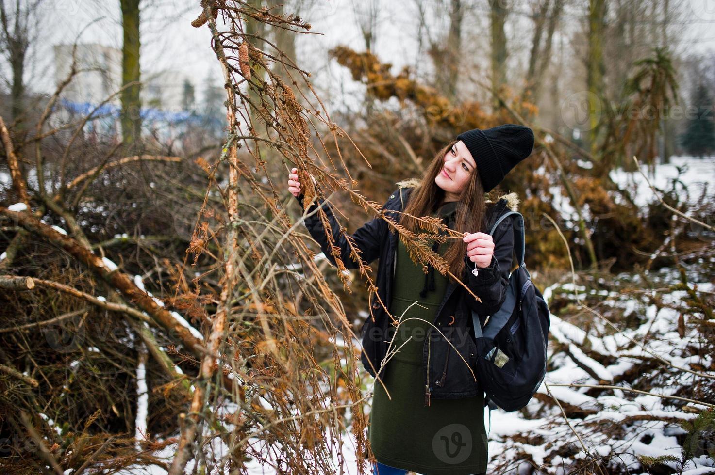 Young girl wear on long green sweatshirt, jeans and black headwear at  branches of the pine tree in winter day. photo