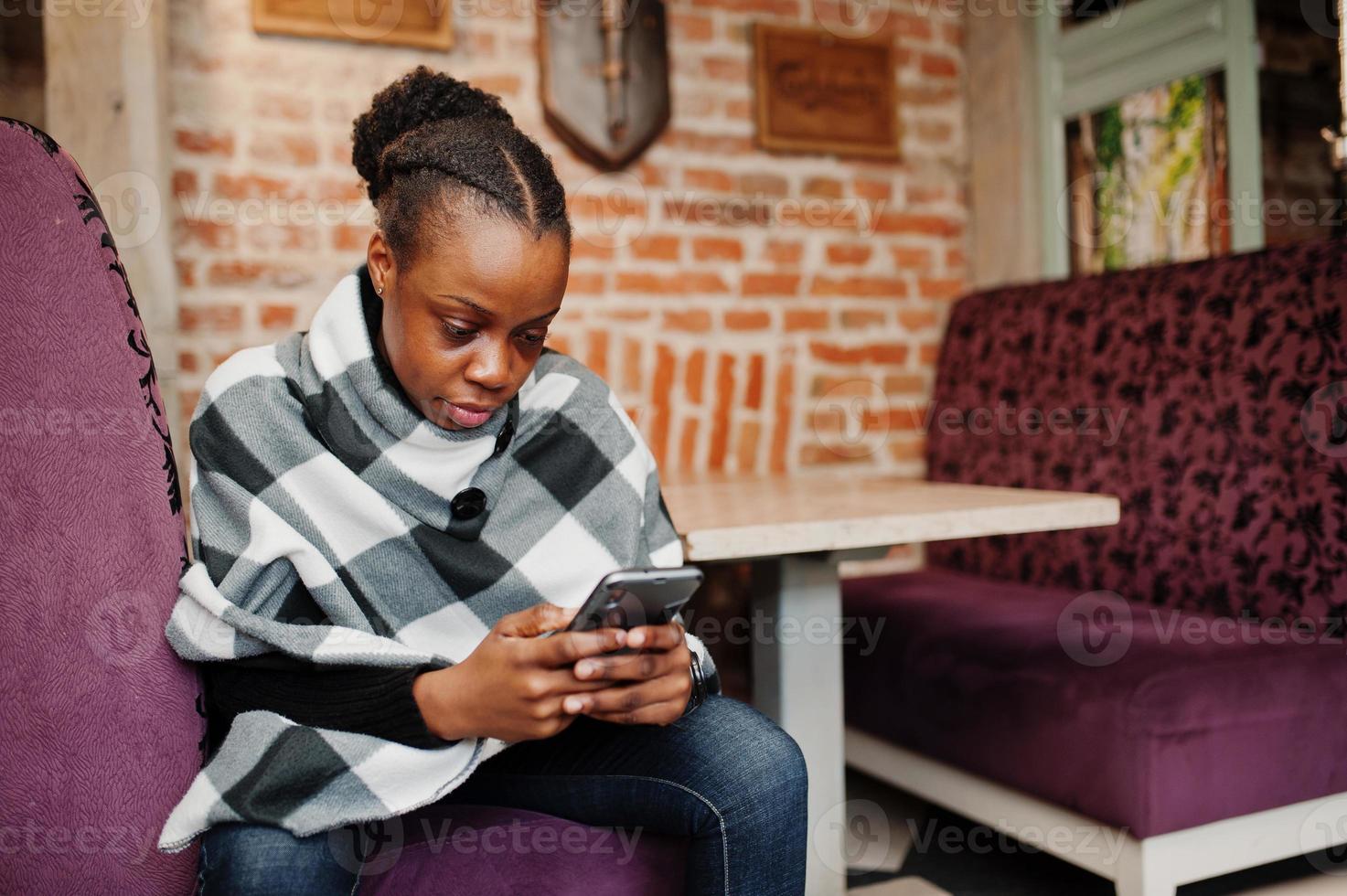 mujer africana en capa a cuadros posó en el café con teléfono móvil en las manos. foto