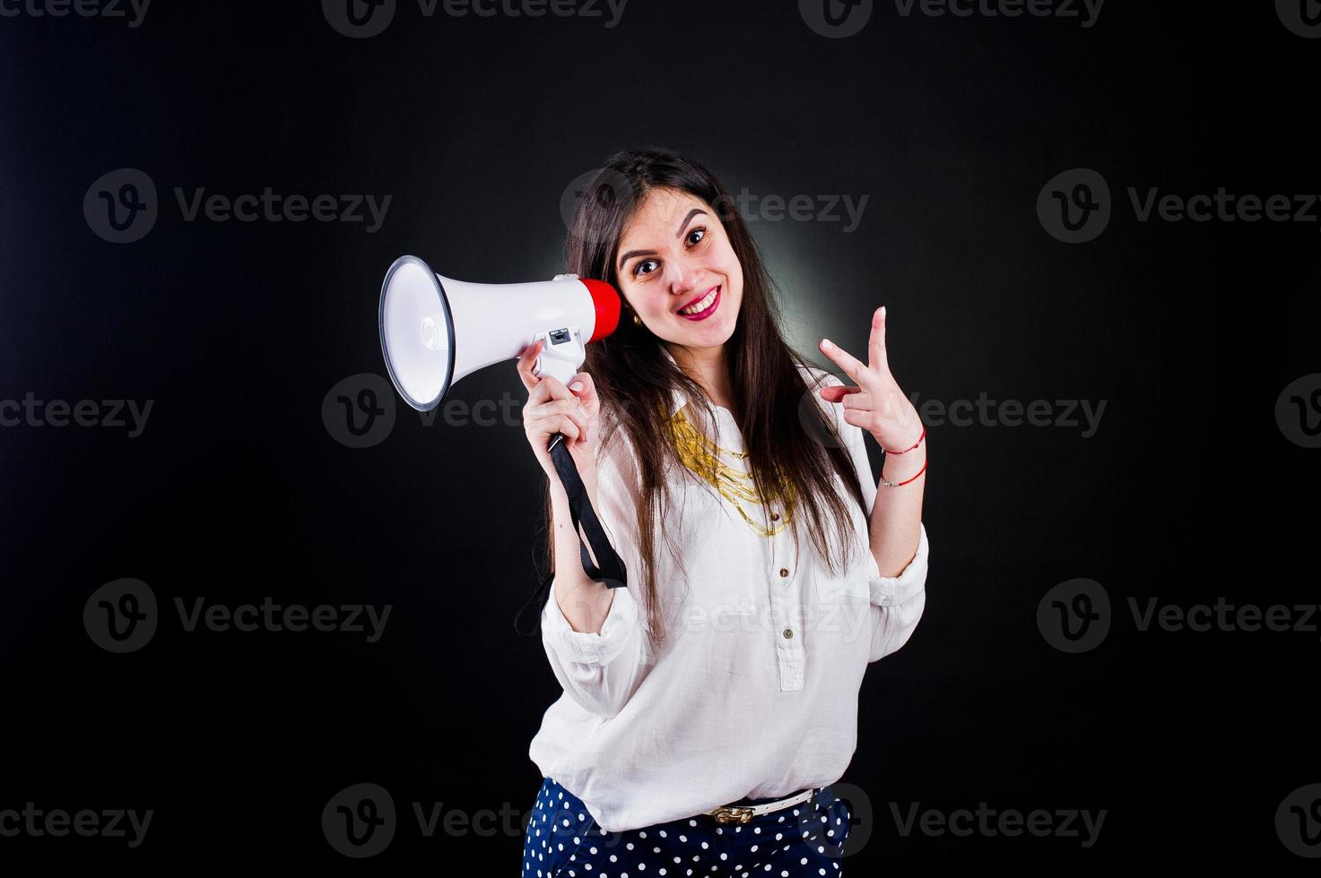 Portrait of a young woman in blue trousers and white blouse posing with megaphone in the studio. photo