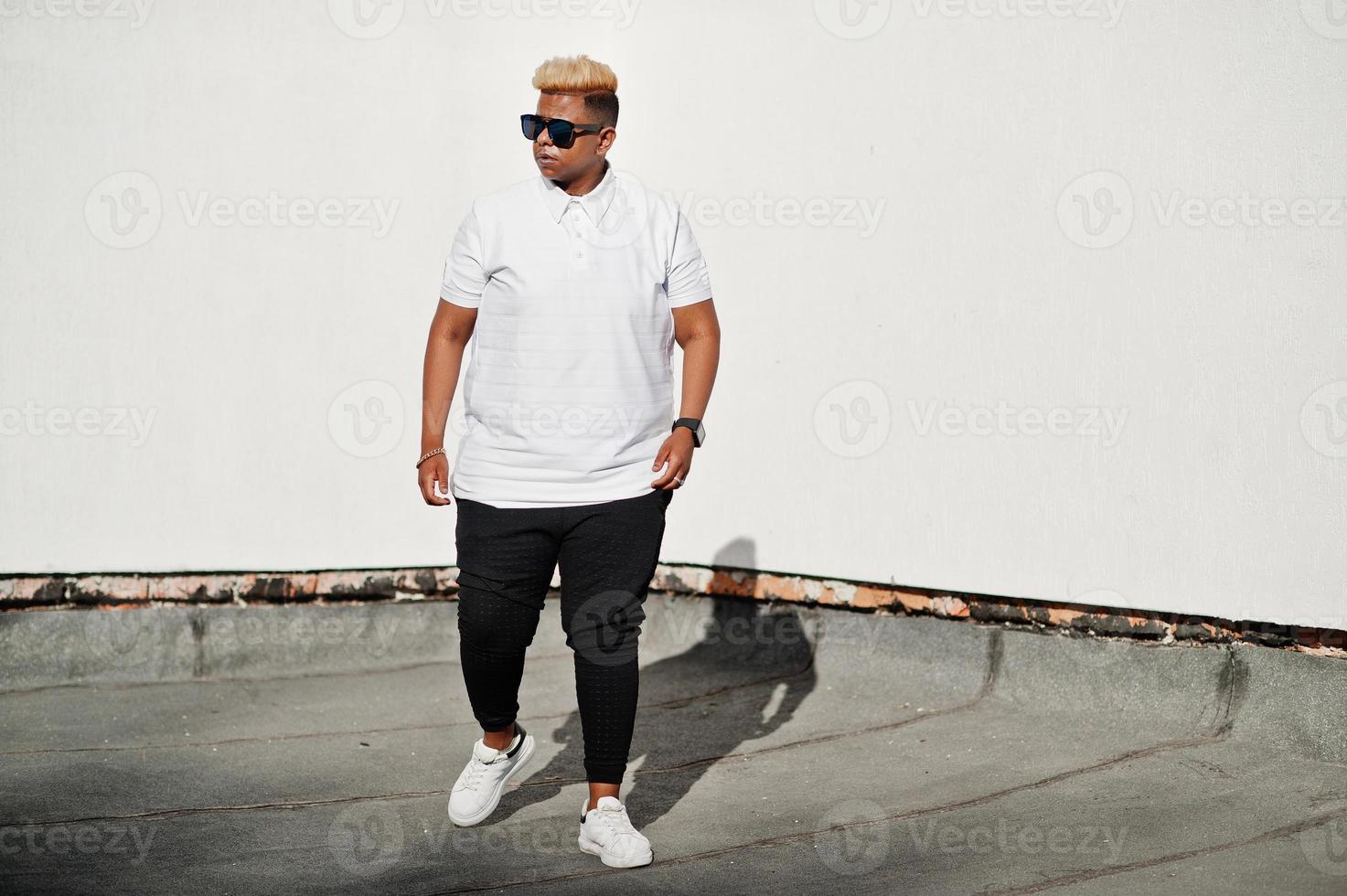 Stylish arabian muslim boy with originally hair and sunglasses posed on streets at roof against white wall. photo