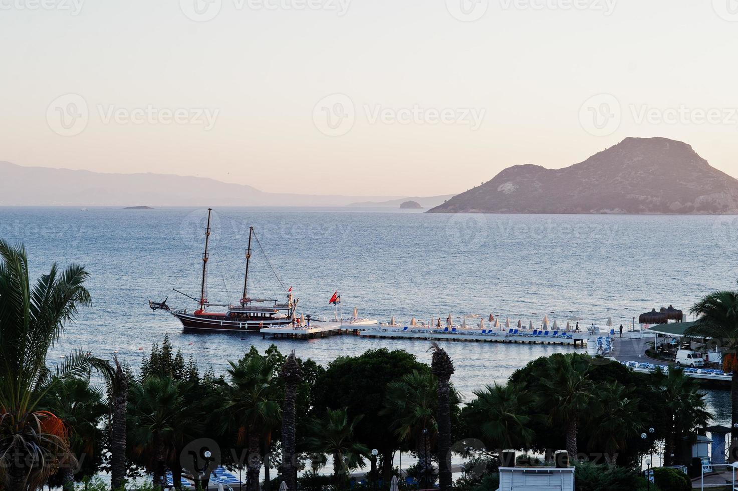 Aerial view of wooden pier with harbor, pirate tourist ship and marina in Turkey resort near Bodrum in sunset light. photo