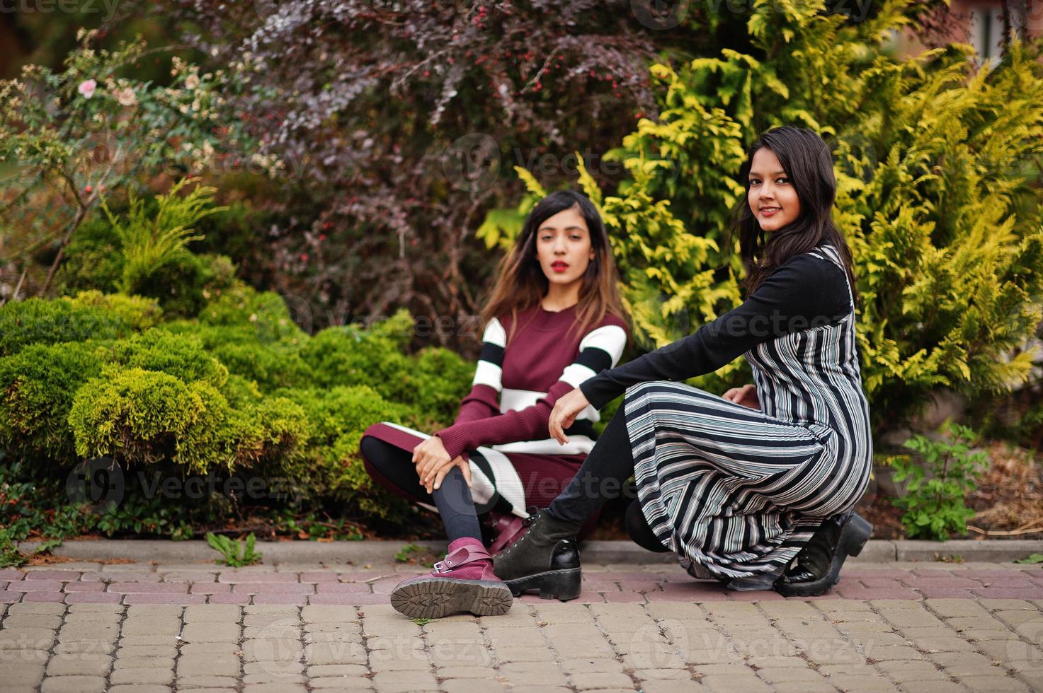 Portrait of two young beautiful indian or south asian teenage girls in dress posed near bushes. photo