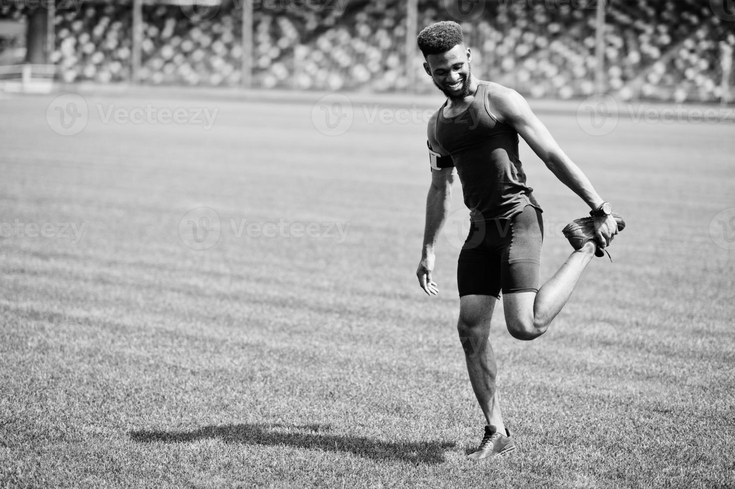 atleta masculino afroamericano en ropa deportiva haciendo ejercicio de estiramiento en el estadio. foto