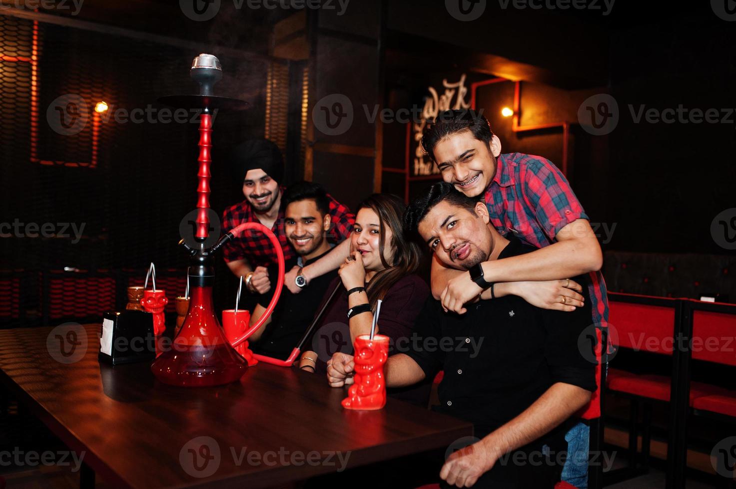 Group of indian friends having fun and rest at night club, drinking cocktails and smoke hookah. photo