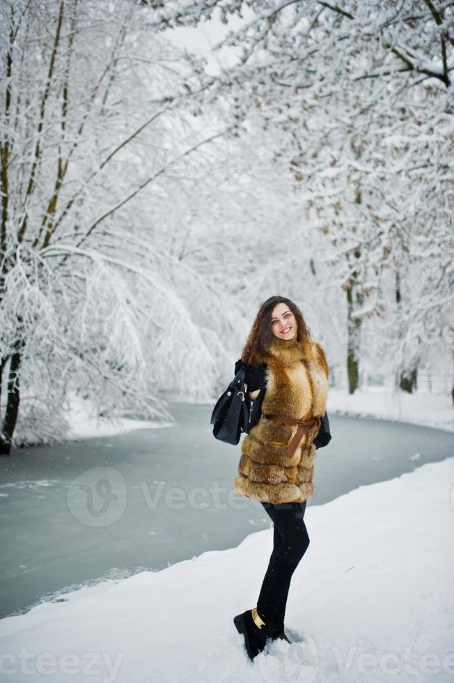 chica rizada de elegancia en abrigo de piel en el parque forestal cubierto de nieve en invierno. foto