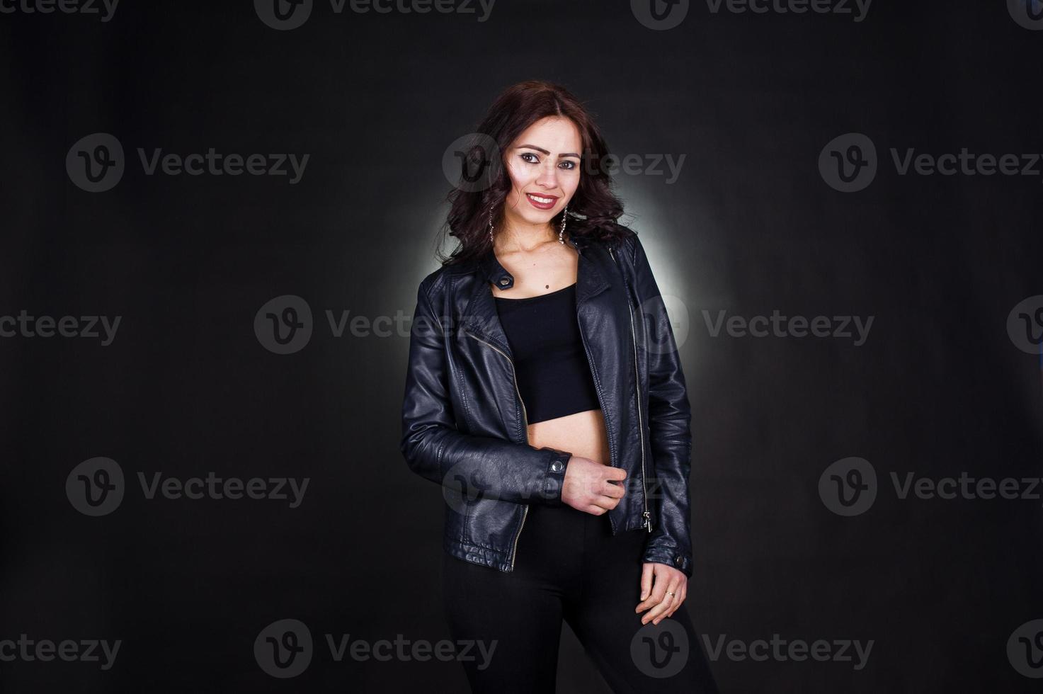 Studio portrait of sexy brunette girl in black leather jacket against black background. photo