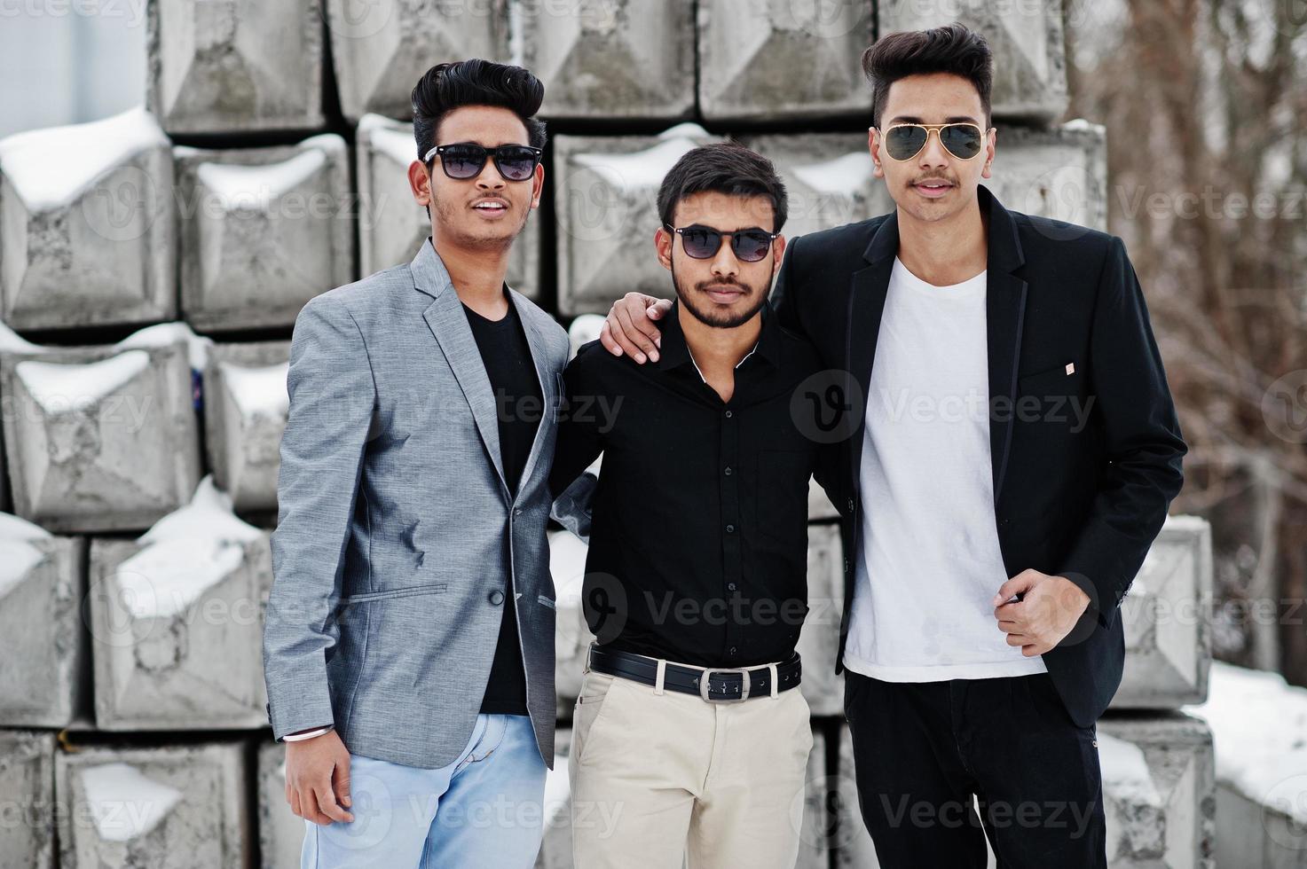 Group of three casual young indian mans in sunglasses posed against stone blocks. photo