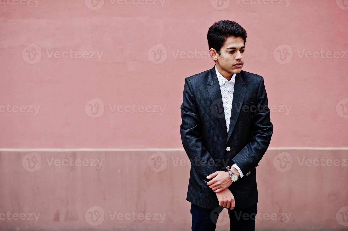 joven indio con traje posado contra una pared rosa. foto