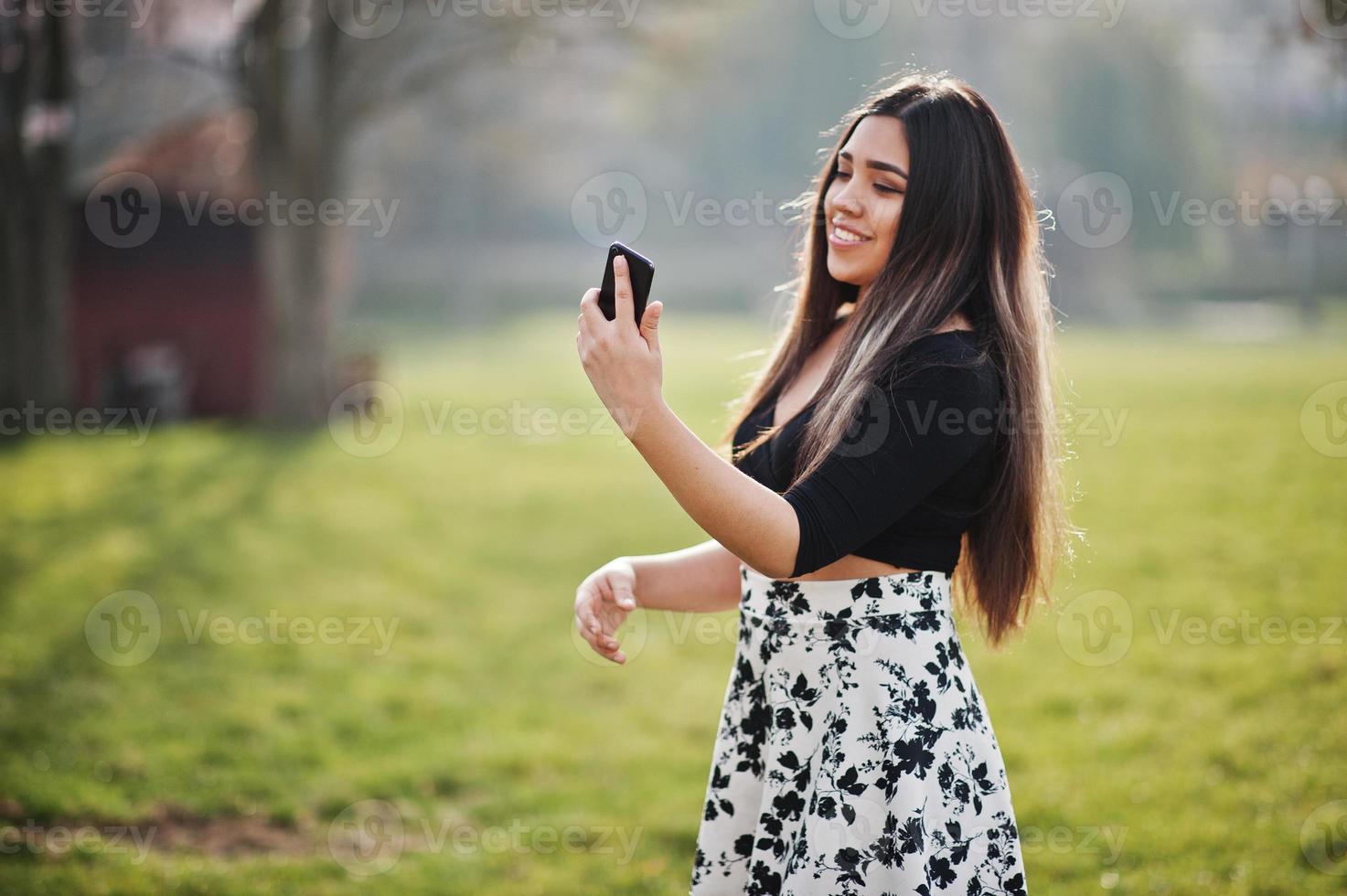 Pretty latino model girl from Ecuador wear on black tops and skirt posed at street with mobile phone. photo