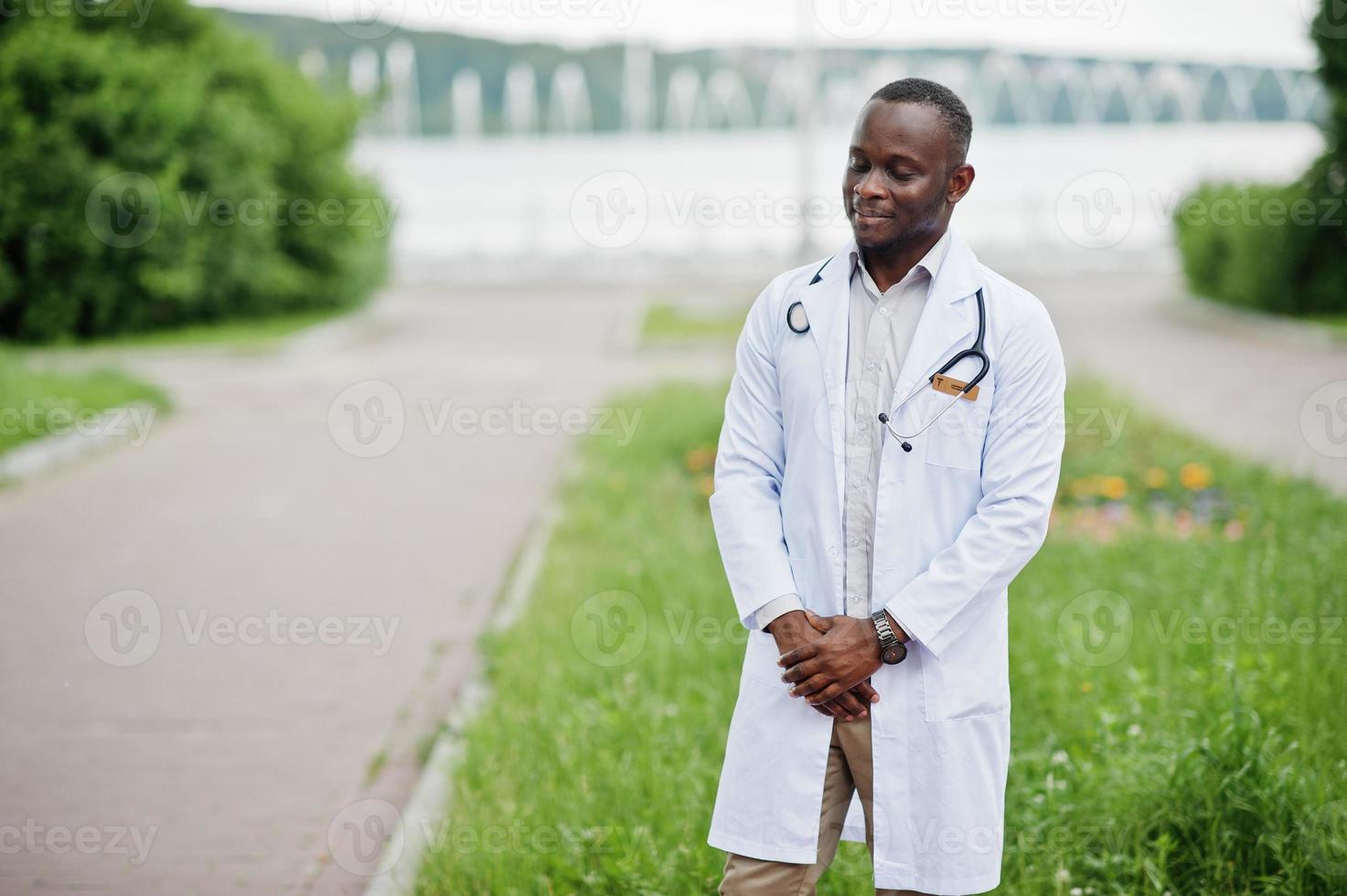 joven médico afroamericano de bata blanca con un estetoscopio posado al aire libre. foto