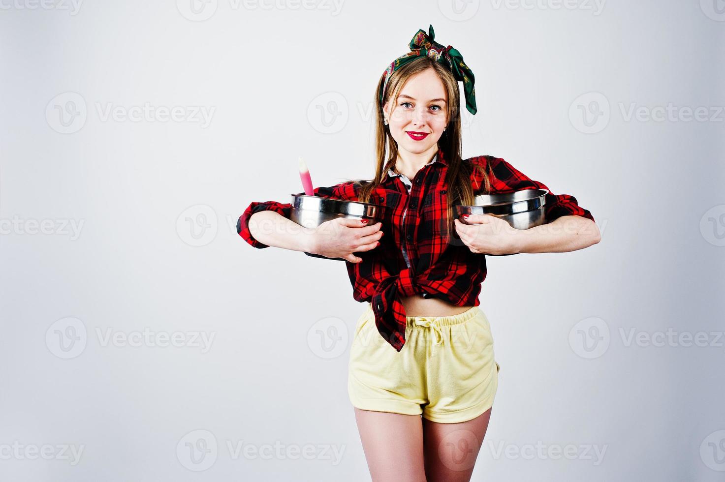 Young funny housewife in checkered shirt and yellow shorts pin up style with two saucepan isolated on white background. photo