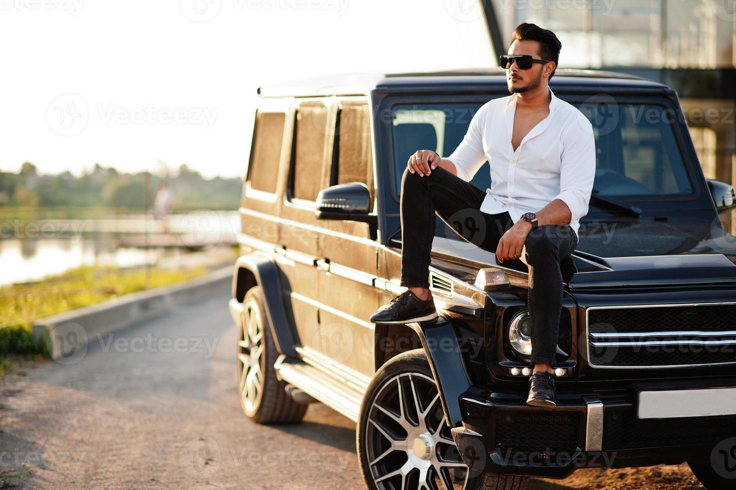 Solid asian man in white shirt and sunglasses posed near black mafia suv car. photo