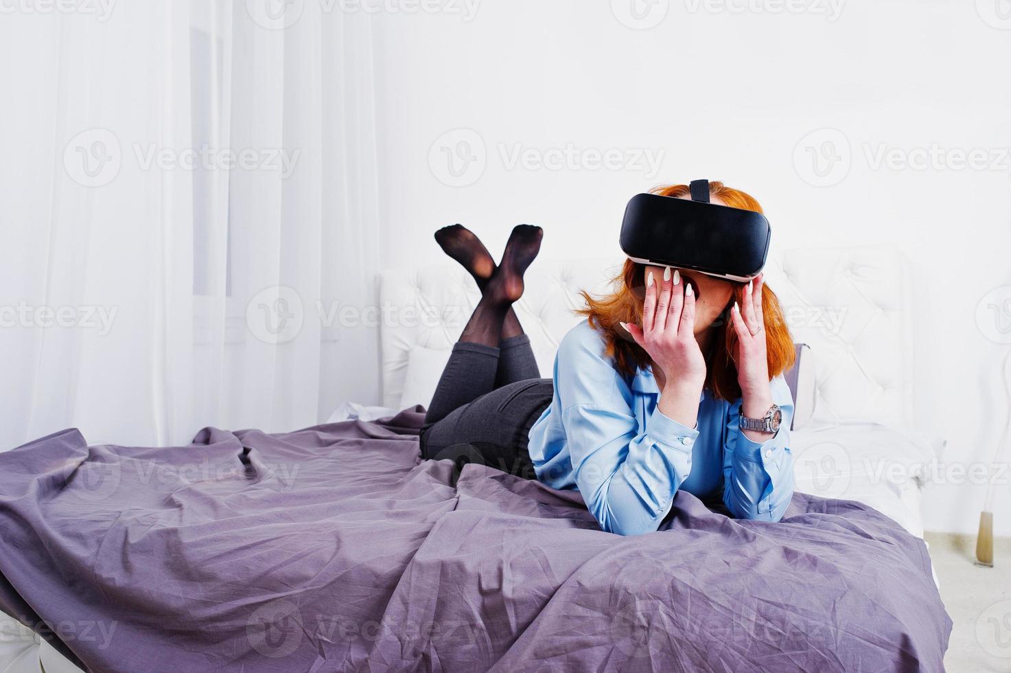Red haired girl in bed with vr glasses at studio room. photo