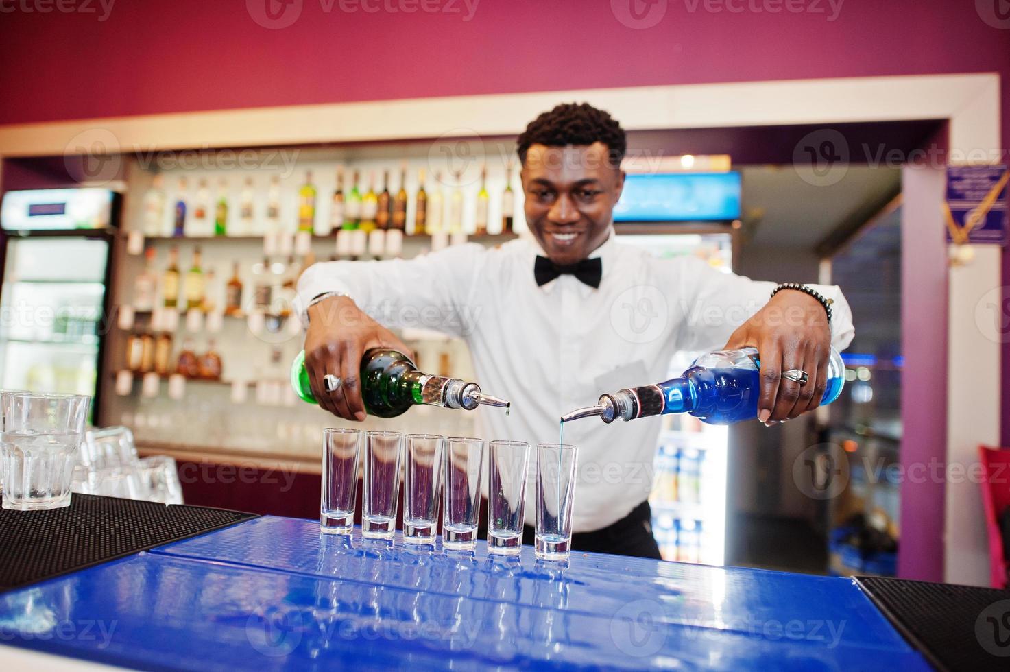 African american bartender at bar making coctails on shots. Alcoholic beverage preparation. photo