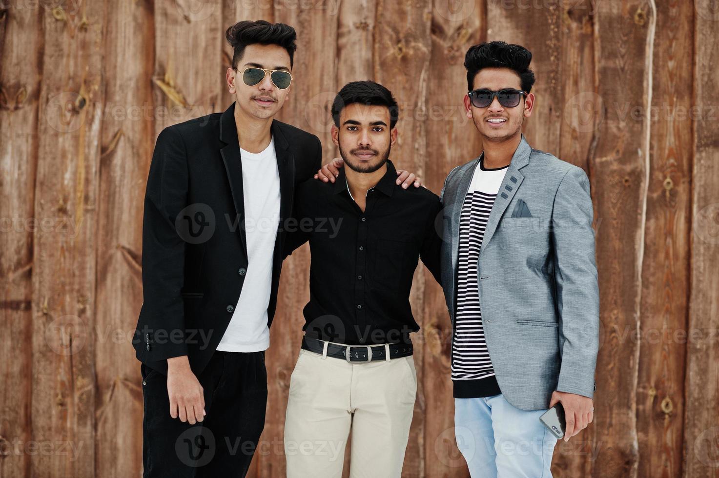 Group of three casual young indian mans posed against wooden background. photo