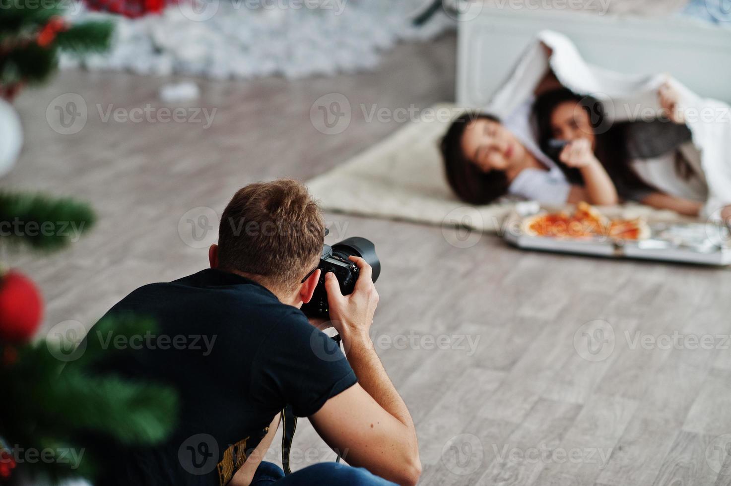 Man photographer shoot on studio twins girls who are eating pizza. Professional photographer on work. photo
