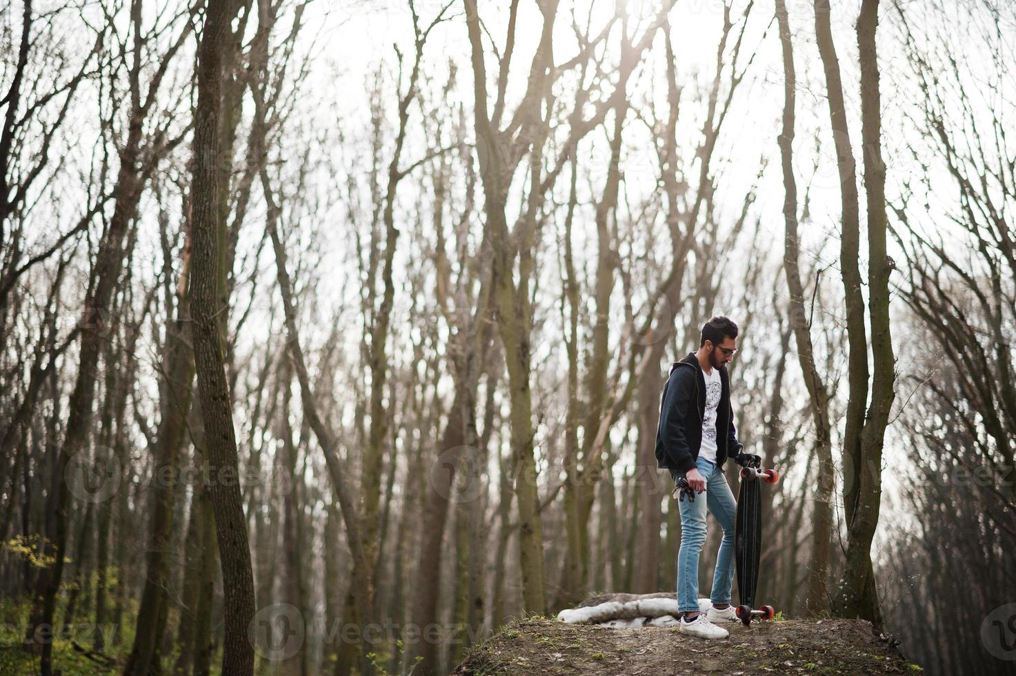 hombre árabe de estilo callejero en anteojos con longboard en madera. foto