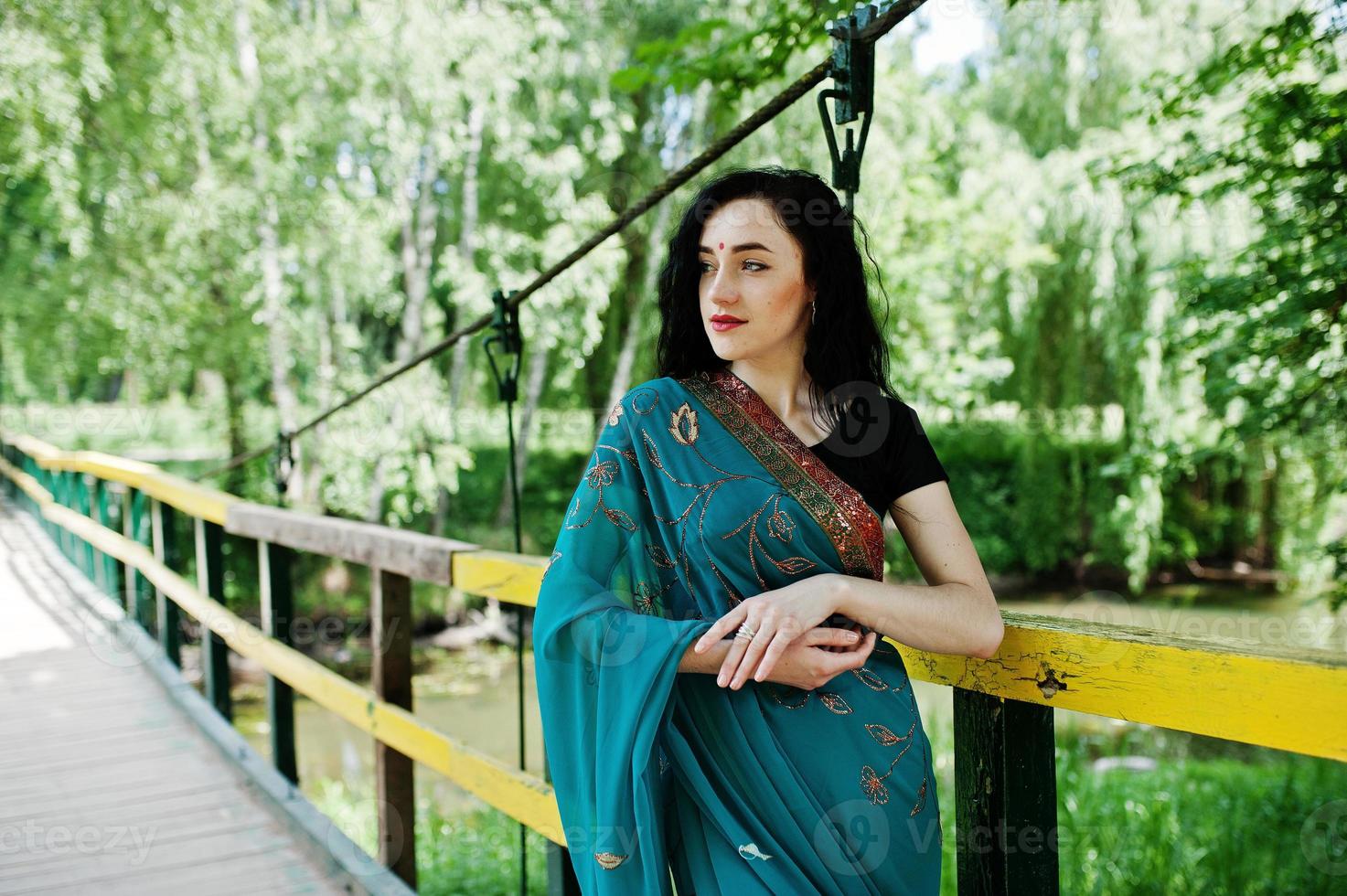 Portrait of beautiful indian brumette girl or hindu woman model on bridge. Traditional Indian costume lehenga choli. photo