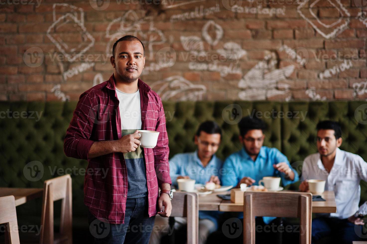 grupo de cuatro hombres del sur de asia posaron en una reunión de negocios en un café. los indios trabajan juntos, conversando. hombre indio con taza de café. foto