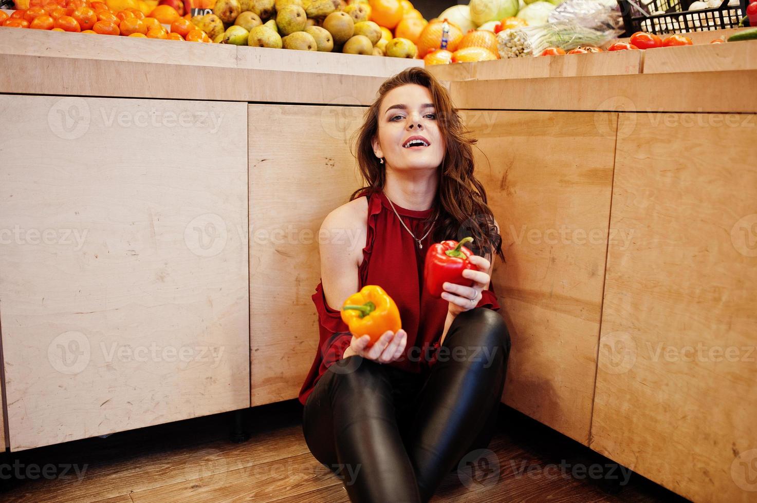 chica de rojo sosteniendo dos pimientos en la tienda de frutas. foto