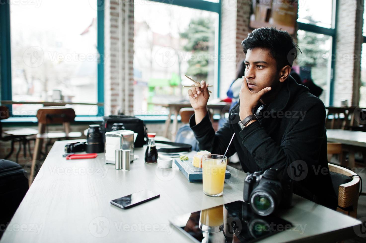 joven asiático casual y elegante con auriculares en el café comiendo sushi. foto